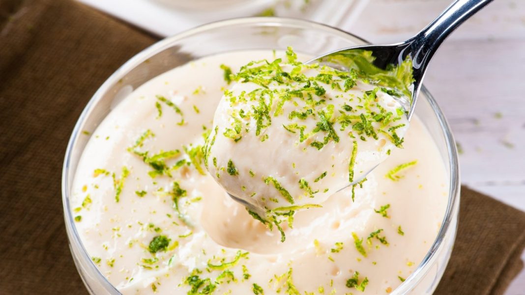 Mousse de limão cremosa sendo servida em uma colher, com raspas de limão por cima, destacando a textura leve e aerada da sobremesa